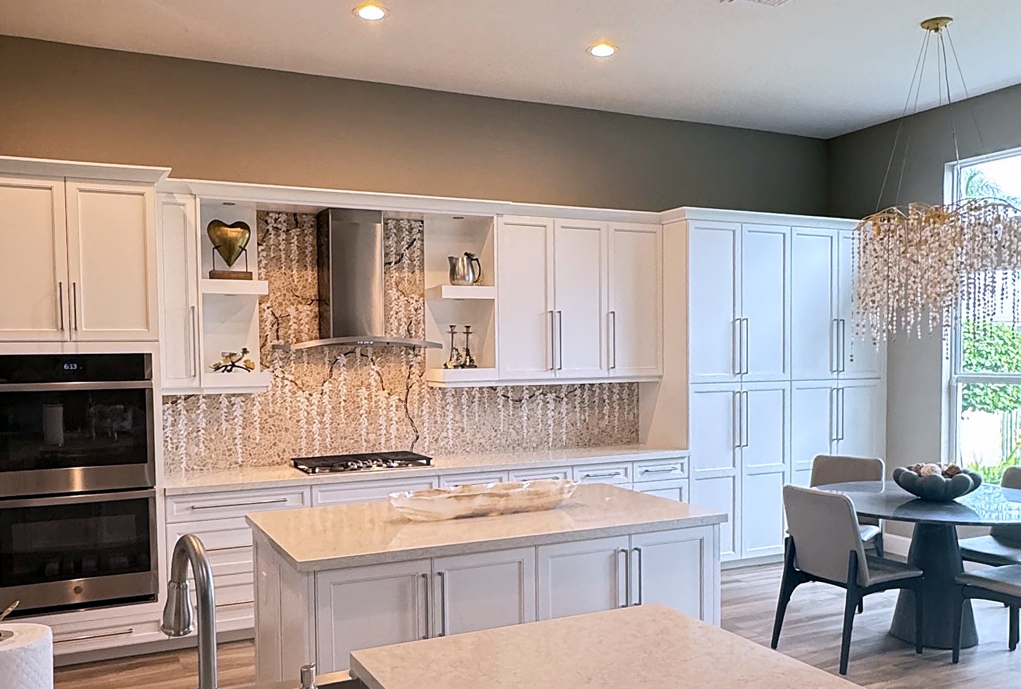 Long white kitchen wall with a marble mosaic wisteria backsplash running behind the range and open shelves